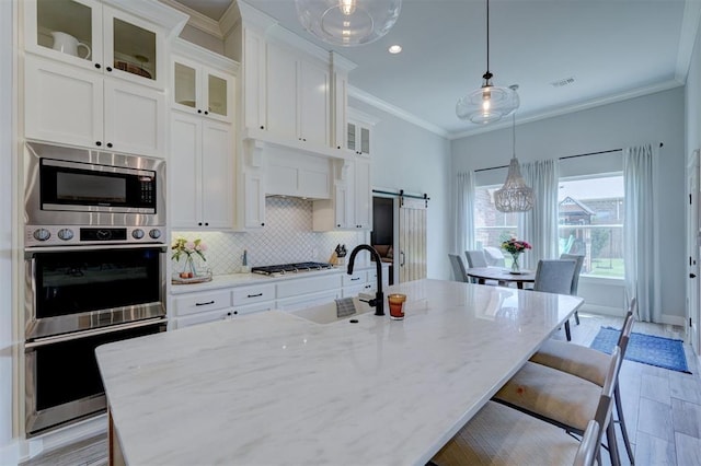 kitchen featuring pendant lighting, white cabinetry, sink, light stone counters, and a barn door