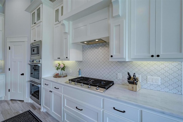 kitchen with light stone counters, tasteful backsplash, light wood-type flooring, stainless steel appliances, and white cabinets