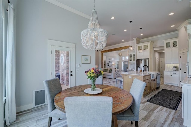 dining room with sink, a notable chandelier, ornamental molding, and light wood-type flooring