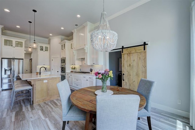 dining room featuring sink, a notable chandelier, ornamental molding, and a barn door