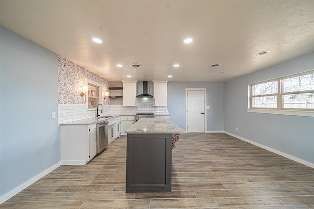 kitchen with a kitchen island, appliances with stainless steel finishes, white cabinetry, sink, and wall chimney range hood