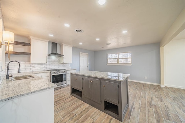 kitchen with white cabinetry, light stone counters, gas range, and wall chimney exhaust hood