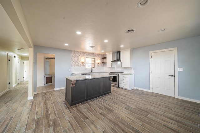 kitchen featuring wall chimney range hood, white cabinetry, stainless steel gas stove, a center island, and tasteful backsplash