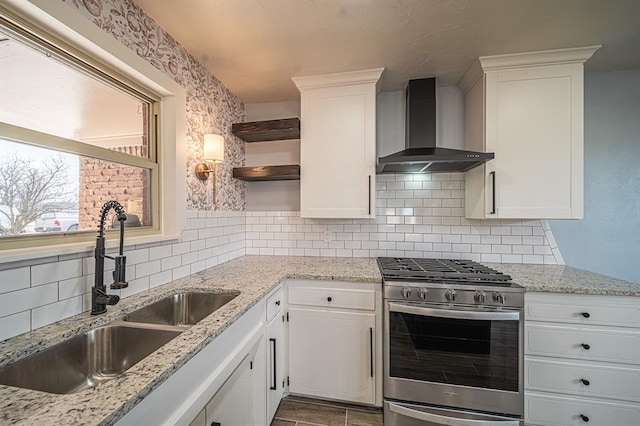 kitchen with sink, gas stove, light stone counters, wall chimney range hood, and white cabinets