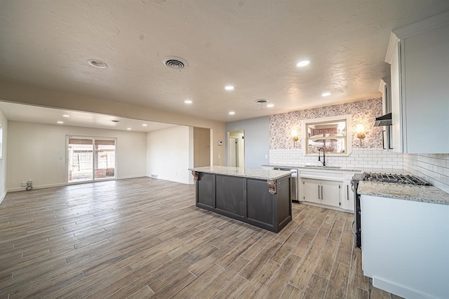 kitchen featuring sink, tasteful backsplash, a center island, light stone countertops, and light hardwood / wood-style floors