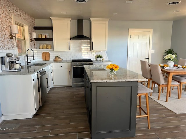 kitchen featuring appliances with stainless steel finishes, white cabinetry, sink, light stone countertops, and wall chimney exhaust hood