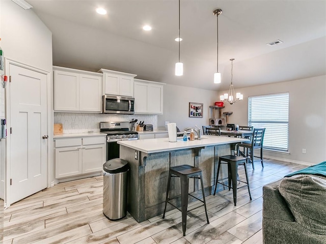 kitchen featuring white cabinetry, stainless steel appliances, hanging light fixtures, and a center island with sink