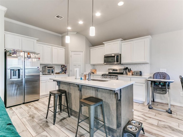 kitchen with white cabinetry, hanging light fixtures, a kitchen island with sink, and appliances with stainless steel finishes