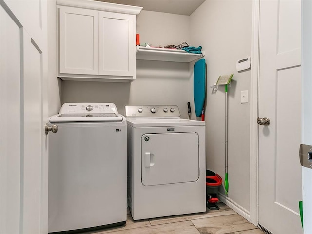 laundry area featuring cabinets, washing machine and dryer, and light hardwood / wood-style flooring