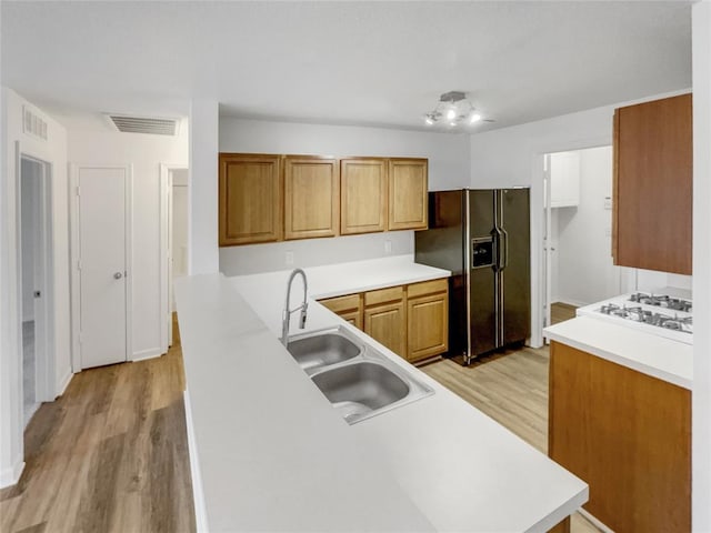 kitchen featuring white gas stovetop, sink, light hardwood / wood-style floors, kitchen peninsula, and black fridge