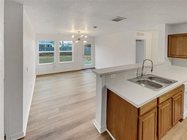 kitchen with sink, a notable chandelier, light hardwood / wood-style floors, kitchen peninsula, and a textured ceiling