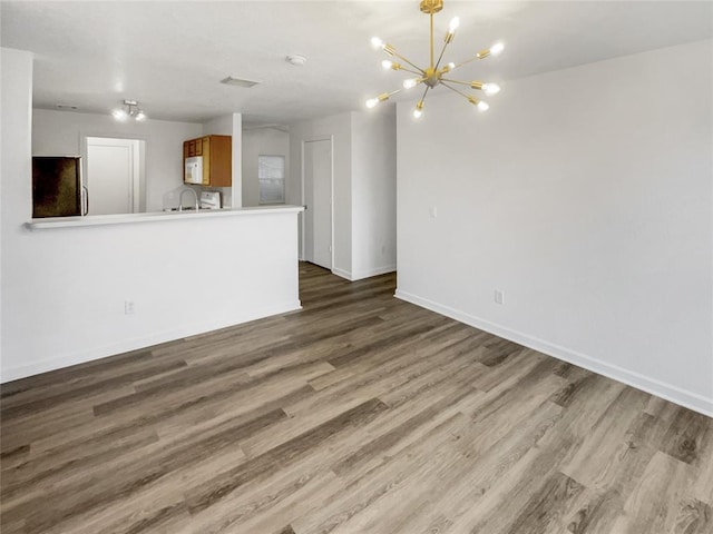 unfurnished living room featuring an inviting chandelier, hardwood / wood-style floors, and sink