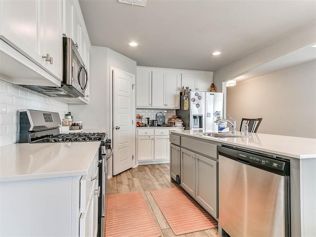 kitchen with sink, white cabinetry, stainless steel appliances, tasteful backsplash, and a center island with sink