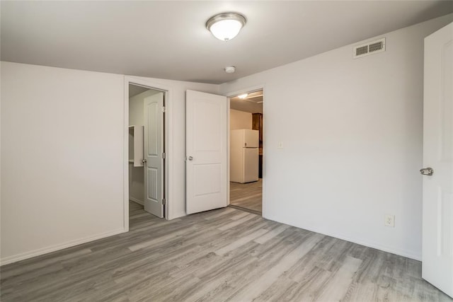 unfurnished bedroom with light hardwood / wood-style floors and white fridge