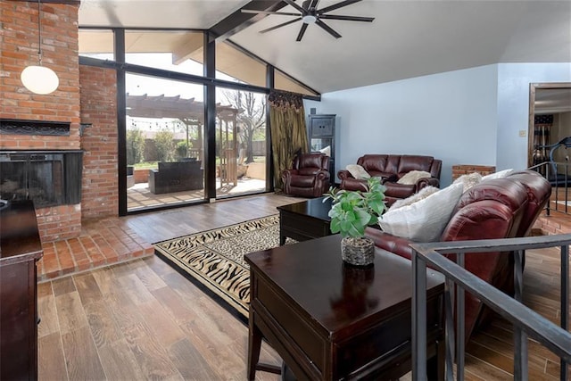 living room with hardwood / wood-style flooring, ceiling fan, lofted ceiling with beams, and a brick fireplace