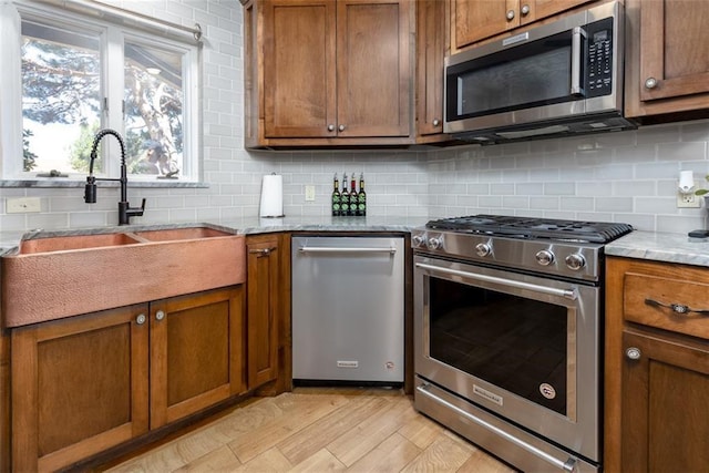 kitchen featuring tasteful backsplash, sink, light stone countertops, and appliances with stainless steel finishes