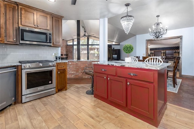 kitchen with vaulted ceiling, appliances with stainless steel finishes, decorative light fixtures, a center island, and light hardwood / wood-style floors