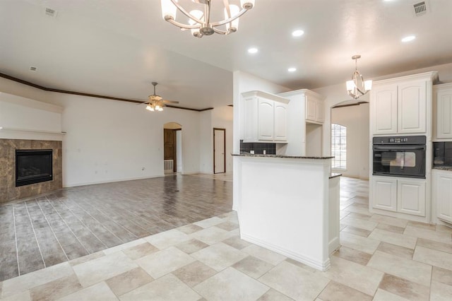 kitchen with white cabinetry, decorative light fixtures, black oven, dark stone counters, and ceiling fan with notable chandelier