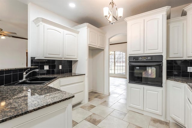 kitchen featuring sink, oven, white cabinets, ceiling fan with notable chandelier, and dark stone counters