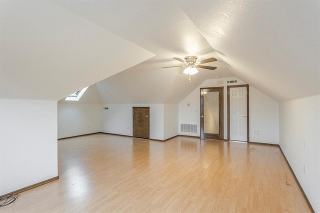 bonus room with ceiling fan, light hardwood / wood-style floors, and vaulted ceiling with skylight