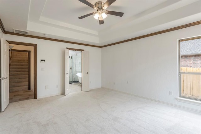 unfurnished bedroom with ensuite bathroom, ornamental molding, light colored carpet, ceiling fan, and a tray ceiling