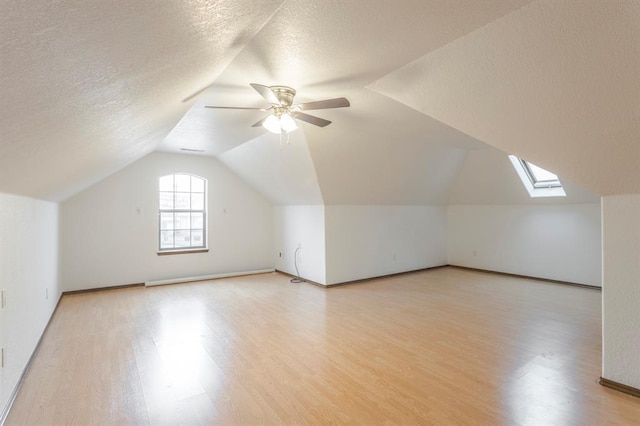 bonus room with ceiling fan, vaulted ceiling with skylight, light hardwood / wood-style flooring, and a textured ceiling