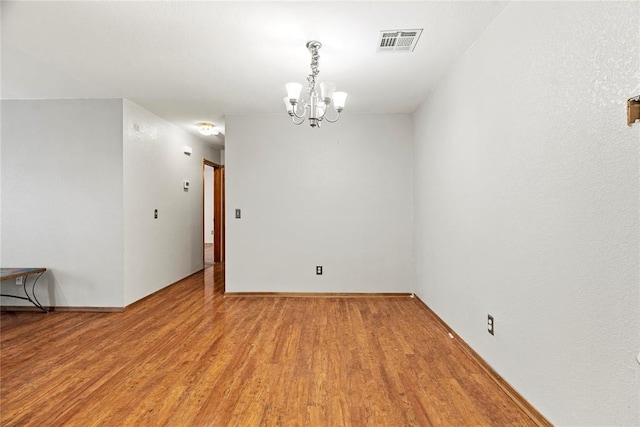 empty room with hardwood / wood-style flooring and a notable chandelier