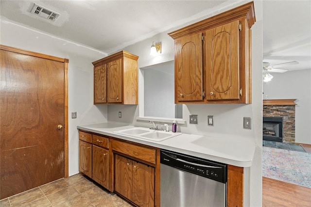 kitchen with ceiling fan, a stone fireplace, dishwasher, and sink