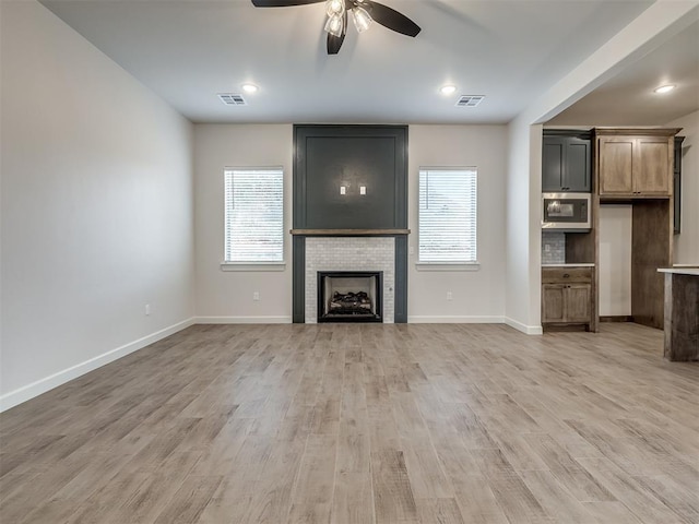 unfurnished living room with ceiling fan, a healthy amount of sunlight, a fireplace, and light hardwood / wood-style flooring