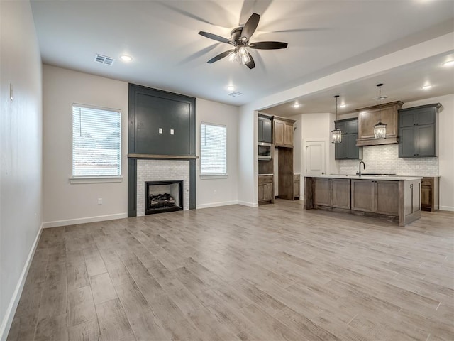 unfurnished living room featuring ceiling fan, sink, a fireplace, and light wood-type flooring