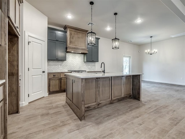 kitchen featuring hanging light fixtures, custom exhaust hood, a center island with sink, and light hardwood / wood-style flooring