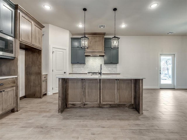 kitchen featuring pendant lighting, sink, a center island with sink, and stainless steel microwave