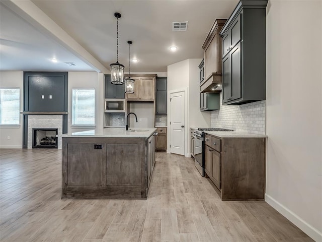 kitchen featuring sink, light hardwood / wood-style flooring, appliances with stainless steel finishes, pendant lighting, and a kitchen island with sink