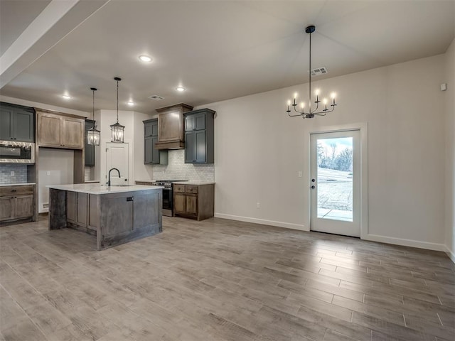 kitchen featuring pendant lighting, an island with sink, wood-type flooring, backsplash, and stainless steel appliances