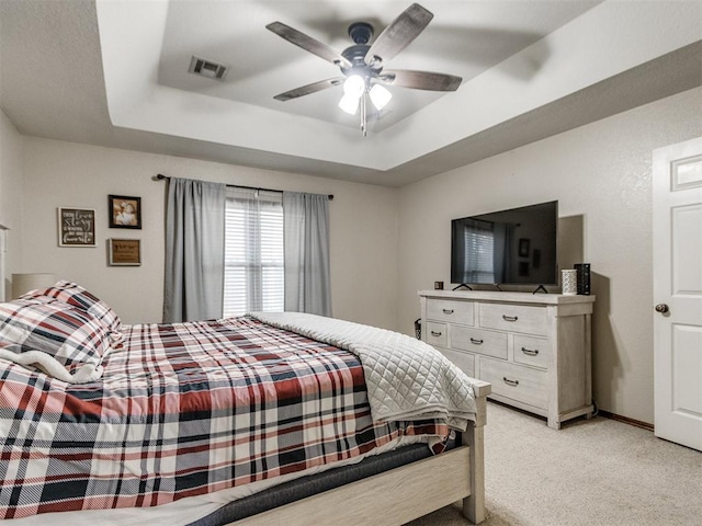 carpeted bedroom featuring ceiling fan and a raised ceiling