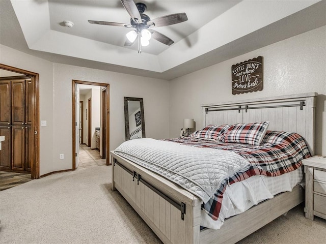 bedroom with a raised ceiling, ensuite bathroom, light carpet, and ceiling fan