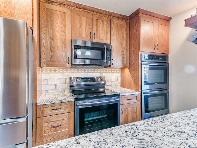 kitchen with tasteful backsplash, light stone counters, and appliances with stainless steel finishes