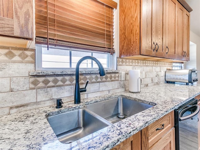 kitchen with tasteful backsplash, dishwasher, sink, and light stone counters