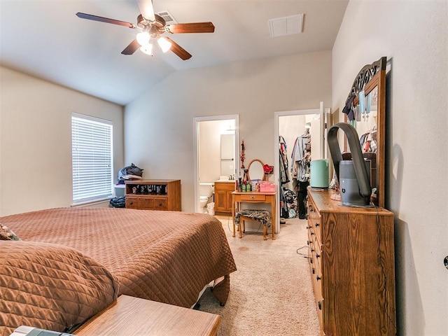 bedroom featuring vaulted ceiling, connected bathroom, a walk in closet, light carpet, and a closet