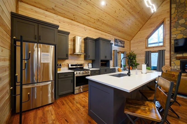 kitchen featuring a breakfast bar, sink, gray cabinetry, stainless steel appliances, and wall chimney range hood