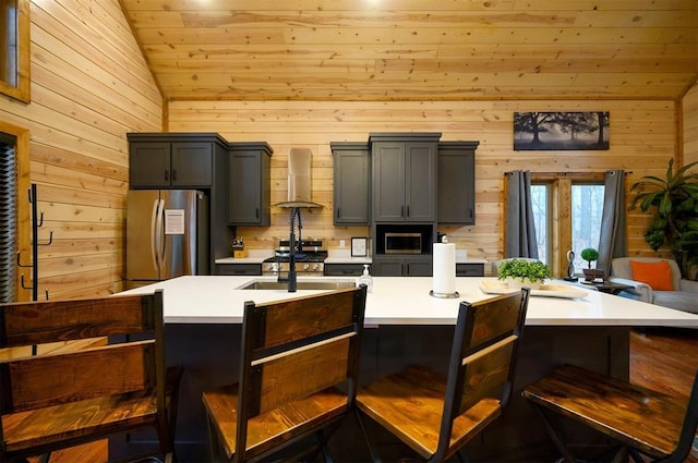 kitchen with wall chimney range hood, a kitchen breakfast bar, an island with sink, and appliances with stainless steel finishes