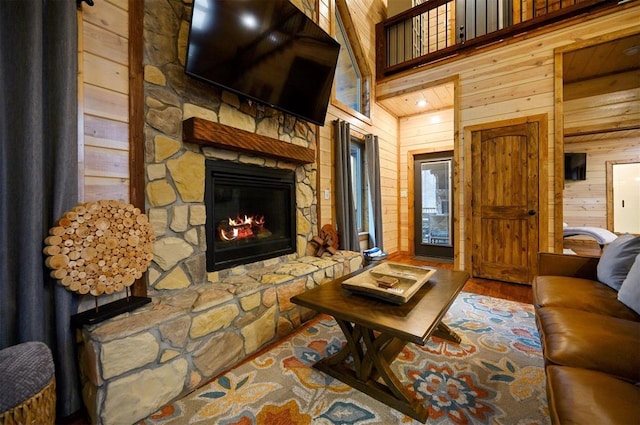 living room featuring a stone fireplace, wooden walls, wood-type flooring, and a high ceiling