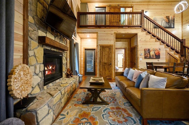 living room with a stone fireplace, a towering ceiling, and wood walls