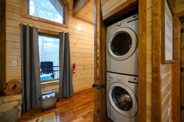 laundry area featuring stacked washing maching and dryer, hardwood / wood-style floors, and wood walls