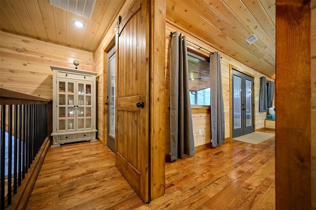 hallway with french doors, wooden walls, light wood-type flooring, and wooden ceiling