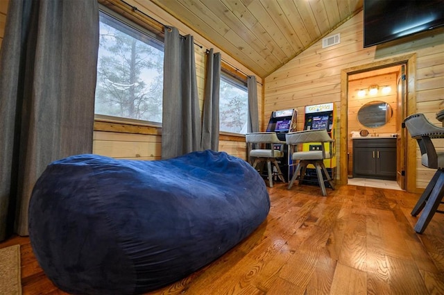 bedroom featuring lofted ceiling, wood ceiling, ensuite bath, light hardwood / wood-style floors, and wood walls