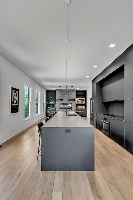 kitchen with light wood-style flooring, modern cabinets, appliances with stainless steel finishes, a kitchen island with sink, and a sink