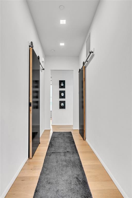 hall with a barn door, light wood-type flooring, and baseboards