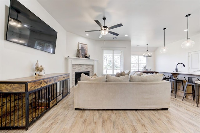 living room featuring a fireplace, ceiling fan with notable chandelier, light hardwood / wood-style flooring, and sink