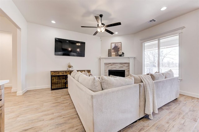 living room with a stone fireplace, light hardwood / wood-style floors, and ceiling fan